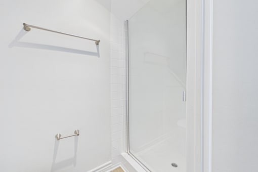 A white bathroom with a glass shower door and a towel bar.