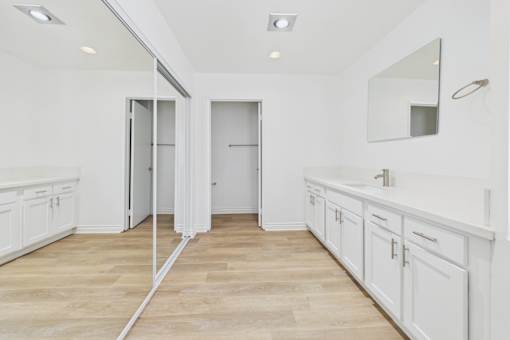 A white bathroom with a wooden floor and a mirror on the wall.