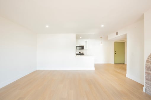 a living room and kitchen with white walls and wood floors