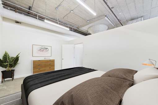 A bedroom with a bed, a plant, and a painting on the wall.