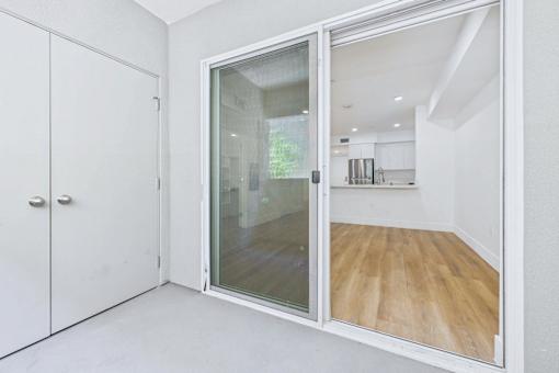 A white room with a glass door leading to a kitchen.