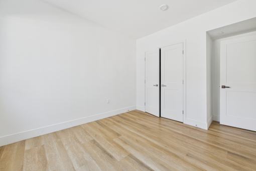 A room with white walls and wooden flooring with two white doors.