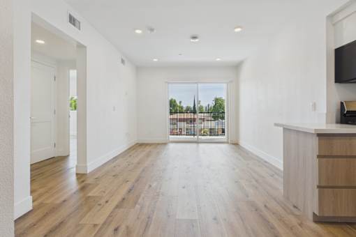 A spacious room with wooden floors and a large window overlooking a balcony.