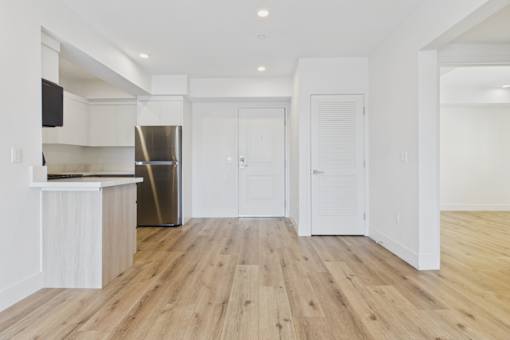 A kitchen with a refrigerator, cabinets, and a wooden floor.