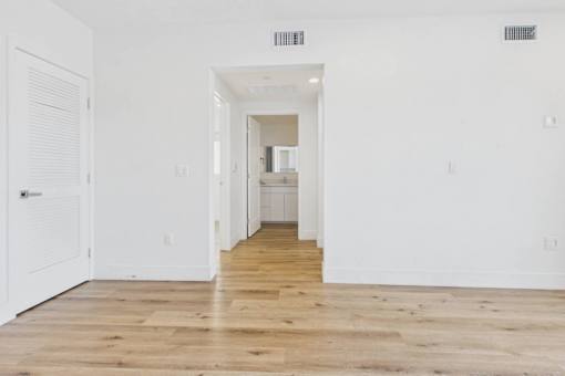 A long white hallway with wood floors and a door on the left.