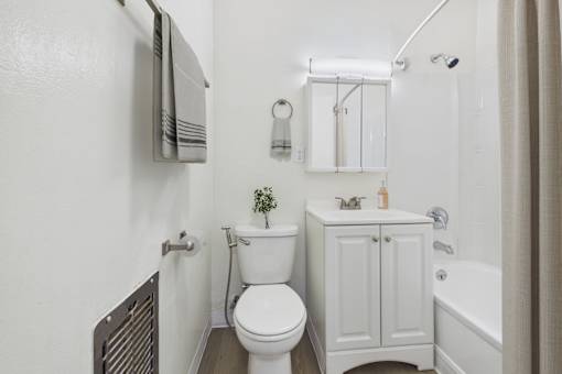 A white toilet sits in a bathroom next to a white cabinet and a white bathtub.