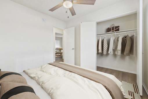 A bedroom with a bed and a closet with clothes hanging.