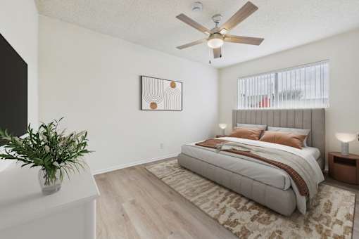 A bedroom with a large bed, a ceiling fan, and a plant on a dresser.