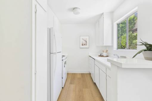 A white kitchen with a refrigerator, cabinets, and a window.