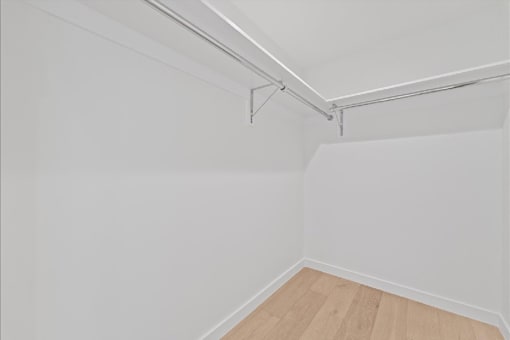 A white wall with a wooden floor and a white ceiling with a metal pipe.