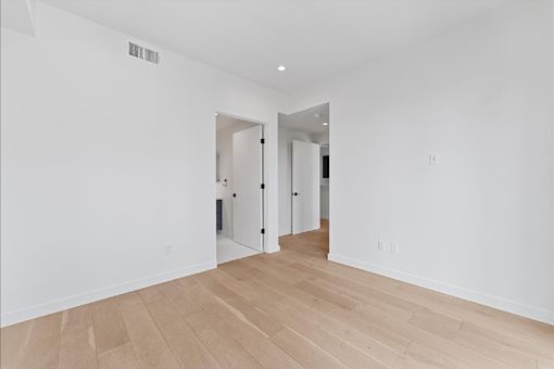 A room with white walls and wooden flooring with a doorway leading to another room.