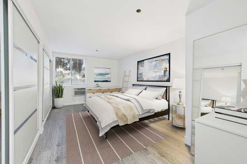 A bedroom with a large bed and a fridge in the corner.
