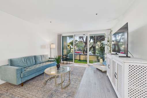 A living room with a blue couch, a glass table, and a television.