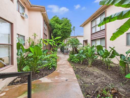 A concrete pathway leads through a lush garden in front of apartment buildings.