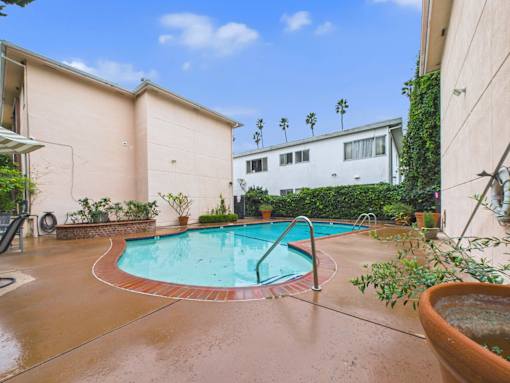 A small pool in a backyard with a white house and palm trees in the background.