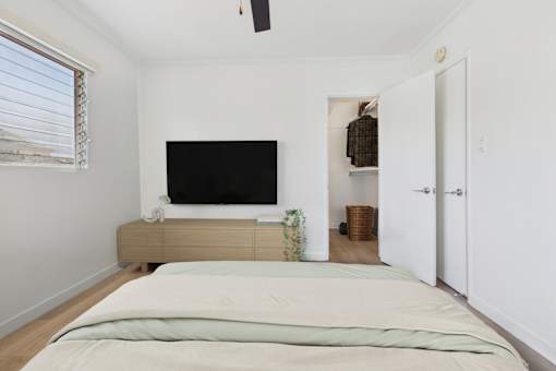A bedroom with a bed, a television, and a window with blinds.