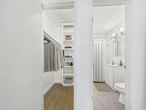 A white bathroom with a toilet, sink, and a closet with a grey robe hanging.