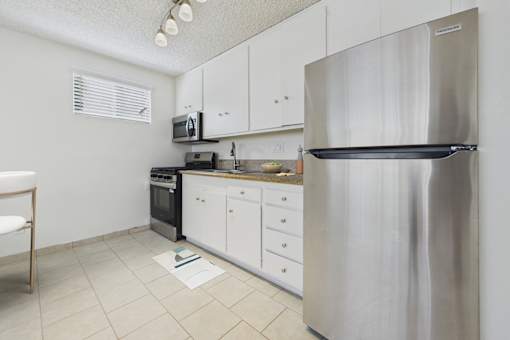 A kitchen with a stainless steel refrigerator, white cabinets, and a black oven.