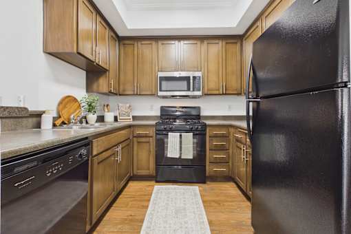 A black refrigerator stands in a kitchen with wooden cabinets and a black oven.