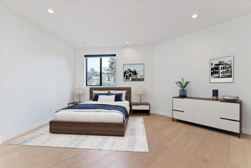 A bedroom with a bed, nightstand, and a dresser with a plant on top.