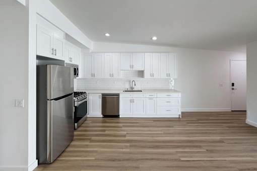 A modern kitchen with white cabinets and a wooden floor.