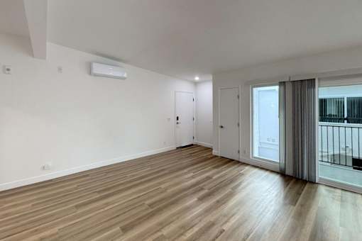A room with wooden flooring and a sliding glass door leading to a balcony.