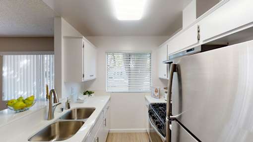 A modern kitchen with a stainless steel refrigerator and a window with blinds.