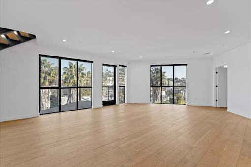 A spacious room with wooden floors and large windows overlooking a cityscape.