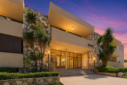A modern building with a stone wall and palm trees in front.