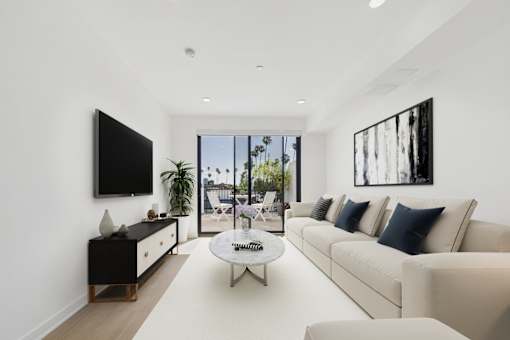 A modern living room with a white sofa, a coffee table, and a flat-screen TV mounted on the wall.