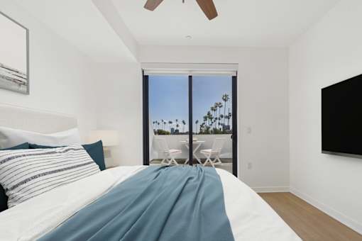A bedroom with a large bed and a view of the outdoors through a sliding glass door.