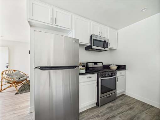 A modern kitchen with a refrigerator, microwave, oven, and a chair.