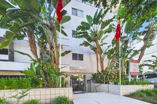 The image shows a building with the name "SHERHOLT" on it, surrounded by green plants and trees.