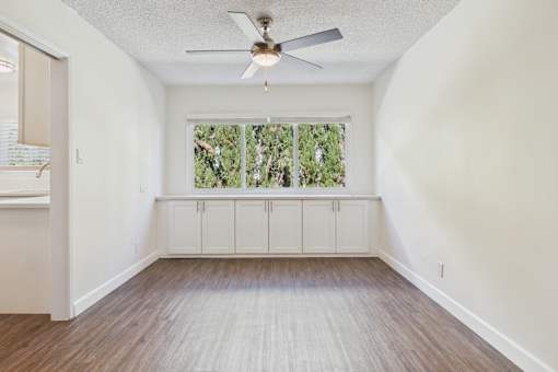 A room with a ceiling fan and a window with a view of trees.