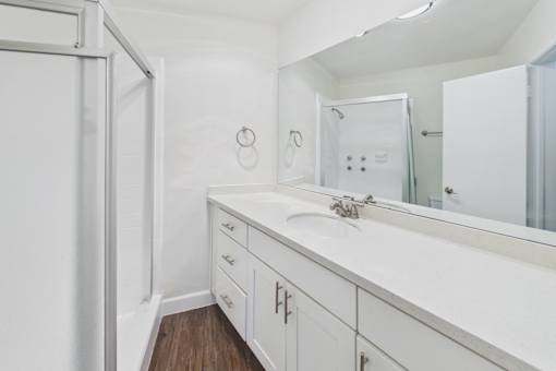 A white bathroom with a sink, mirror, and cabinets.