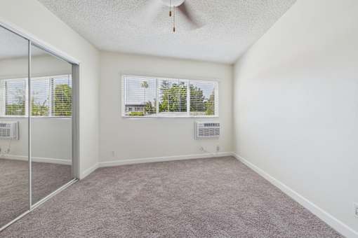 A room with a ceiling fan and two windows.