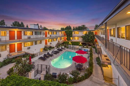 A pool surrounded by lounge chairs and umbrellas is the centerpiece of a courtyard surrounded by apartment buildings.