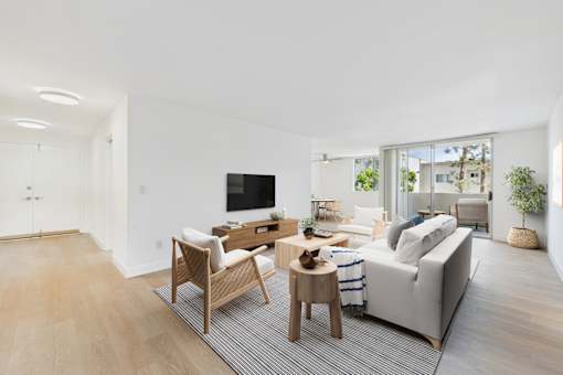 A modern living room with a grey sofa, wooden chairs, and a television.
