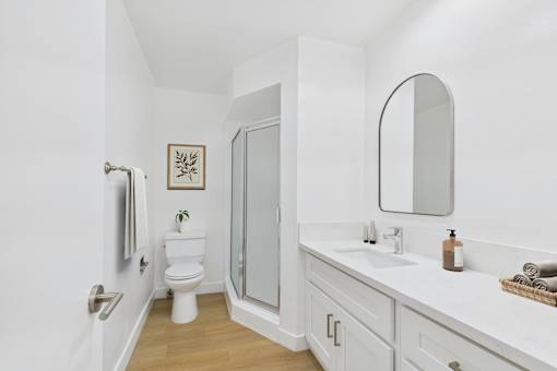 A white bathroom with a toilet, sink, mirror, and shower.