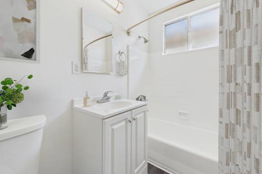 A white bathroom with a sink, mirror, and bathtub.