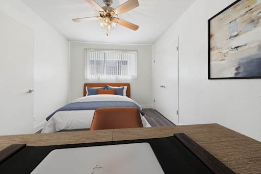 A bedroom with a bed, a ceiling fan, and a painting on the wall.