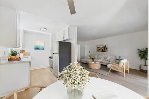 A kitchen with a refrigerator, a dining table with a vase of flowers on it, and a living room with a couch and a coffee table.