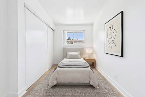 A bedroom with a bed, a window, and a picture on the wall.