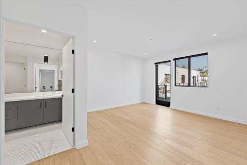 A spacious room with wooden flooring and a view of the city through the windows.