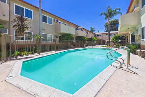 A swimming pool in a residential area surrounded by houses and palm trees.