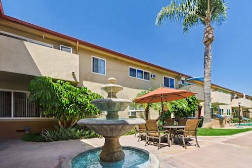 A fountain is in the middle of a patio with chairs and an umbrella.
