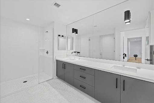 A bathroom with a white sink and grey cabinets.