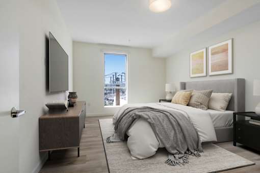 A bedroom with a bed, a dresser, and a window overlooking a cityscape.