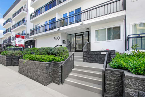 the front entrance of an apartment building with stairs and a sidewalk