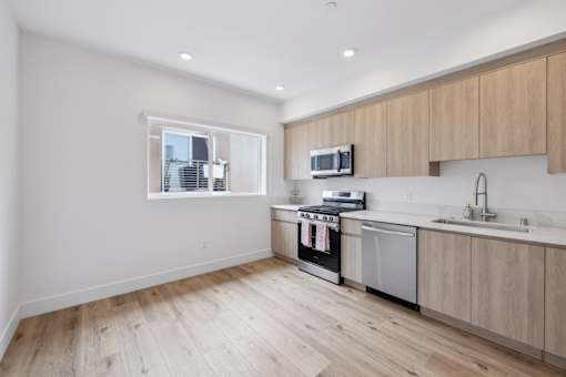 A kitchen with wooden floors and cabinets, a window, and modern appliances.